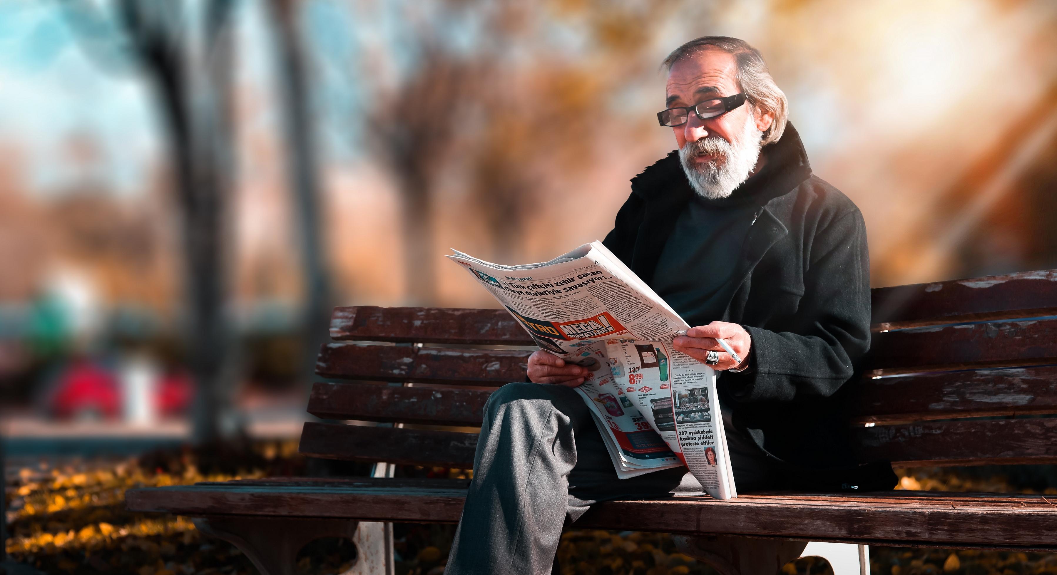 man sitting on park bench reading the newspaper